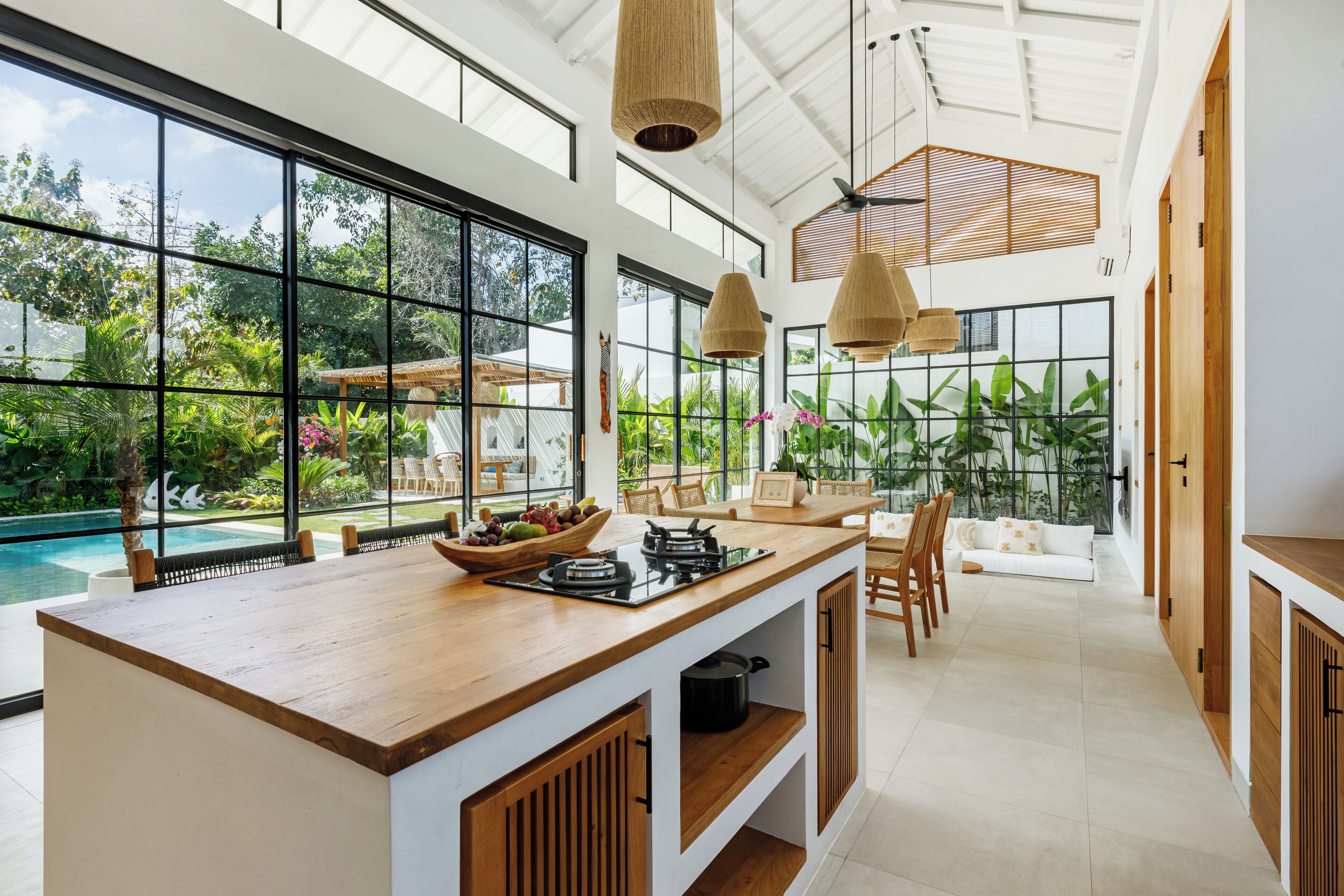A spacious kitchen with a large island, wooden cabinets, and a view of a swimming pool and lush greenery.