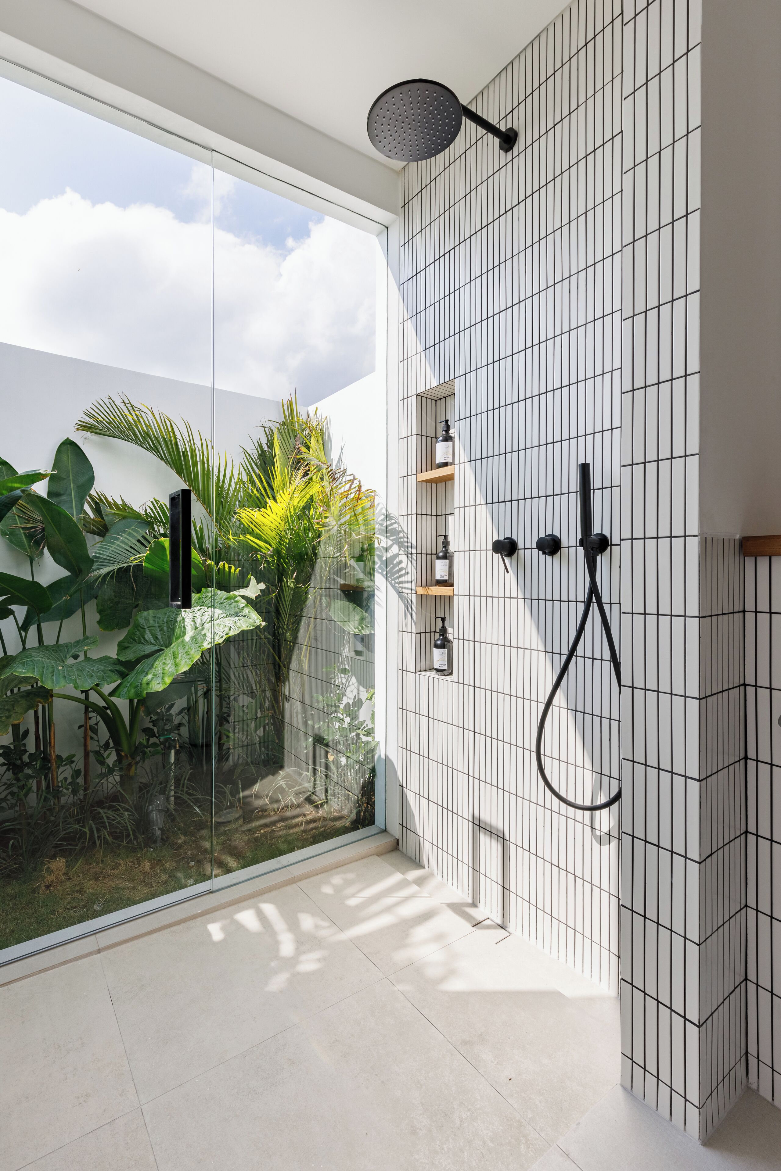 Een moderne badkamer met een douchecabine van glas, witte betegelde wanden en uitzicht op groen.