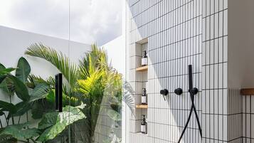 Een moderne badkamer met een douchecabine van glas, witte betegelde wanden en uitzicht op groen.