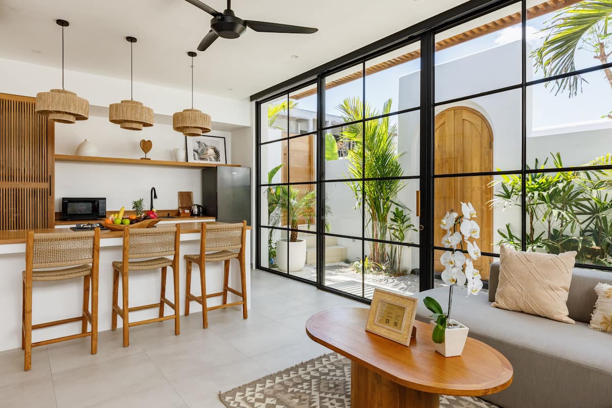 A modern kitchen with a dining area, large windows, and a view of the outdoors.