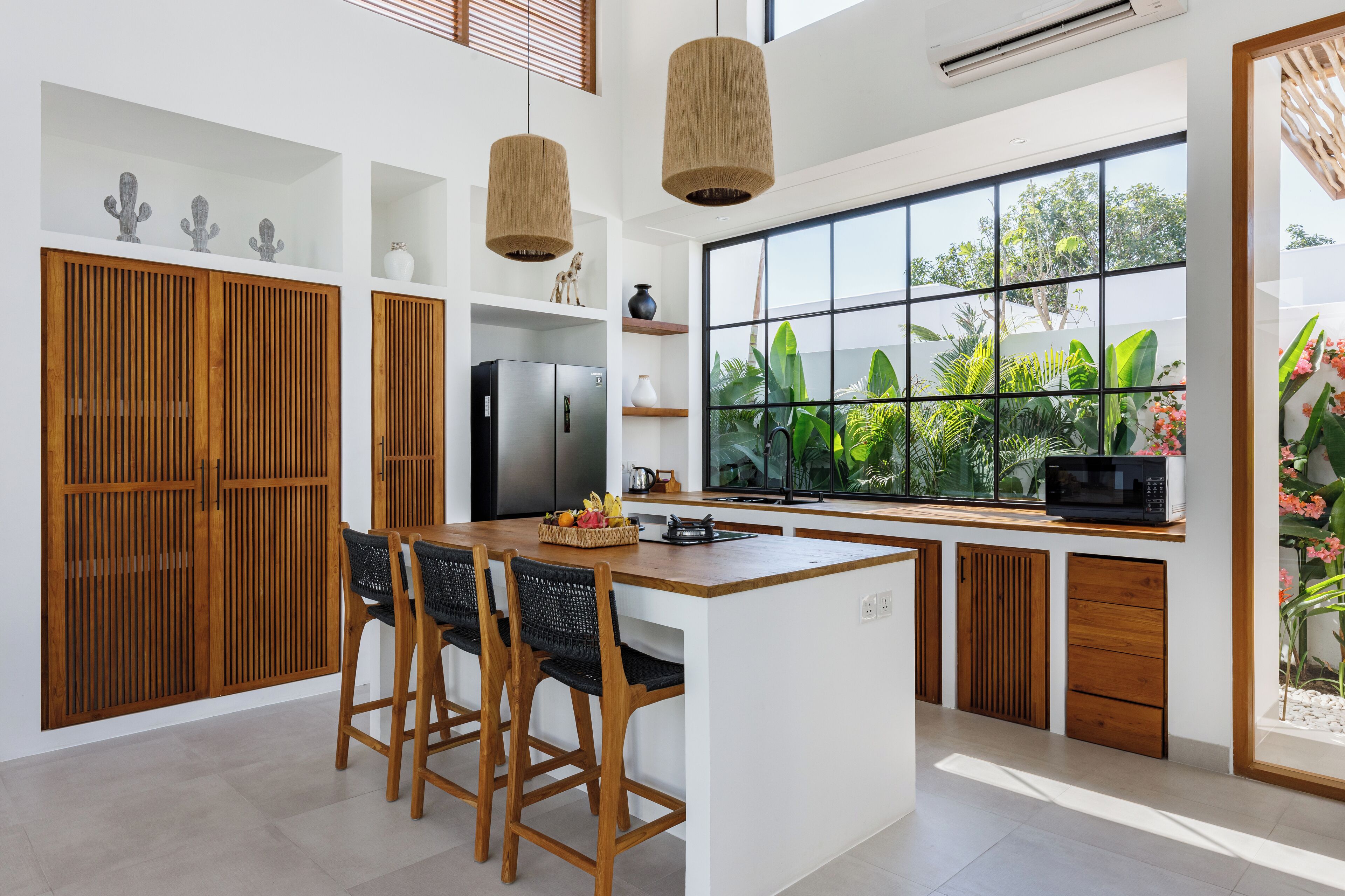 A modern kitchen with a central island, wooden cabinets, and a large window with a view of greenery.