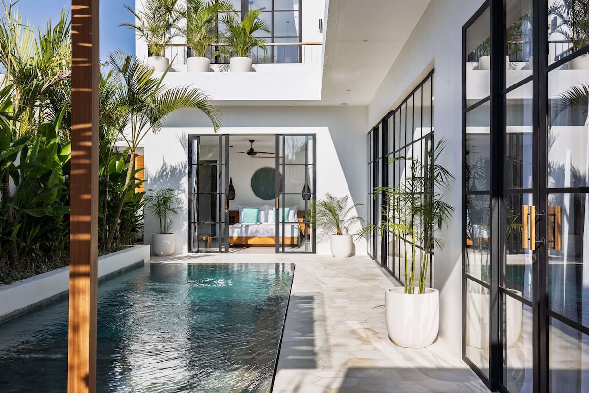 A modern hotel interior with a pool, large windows, and indoor plants.