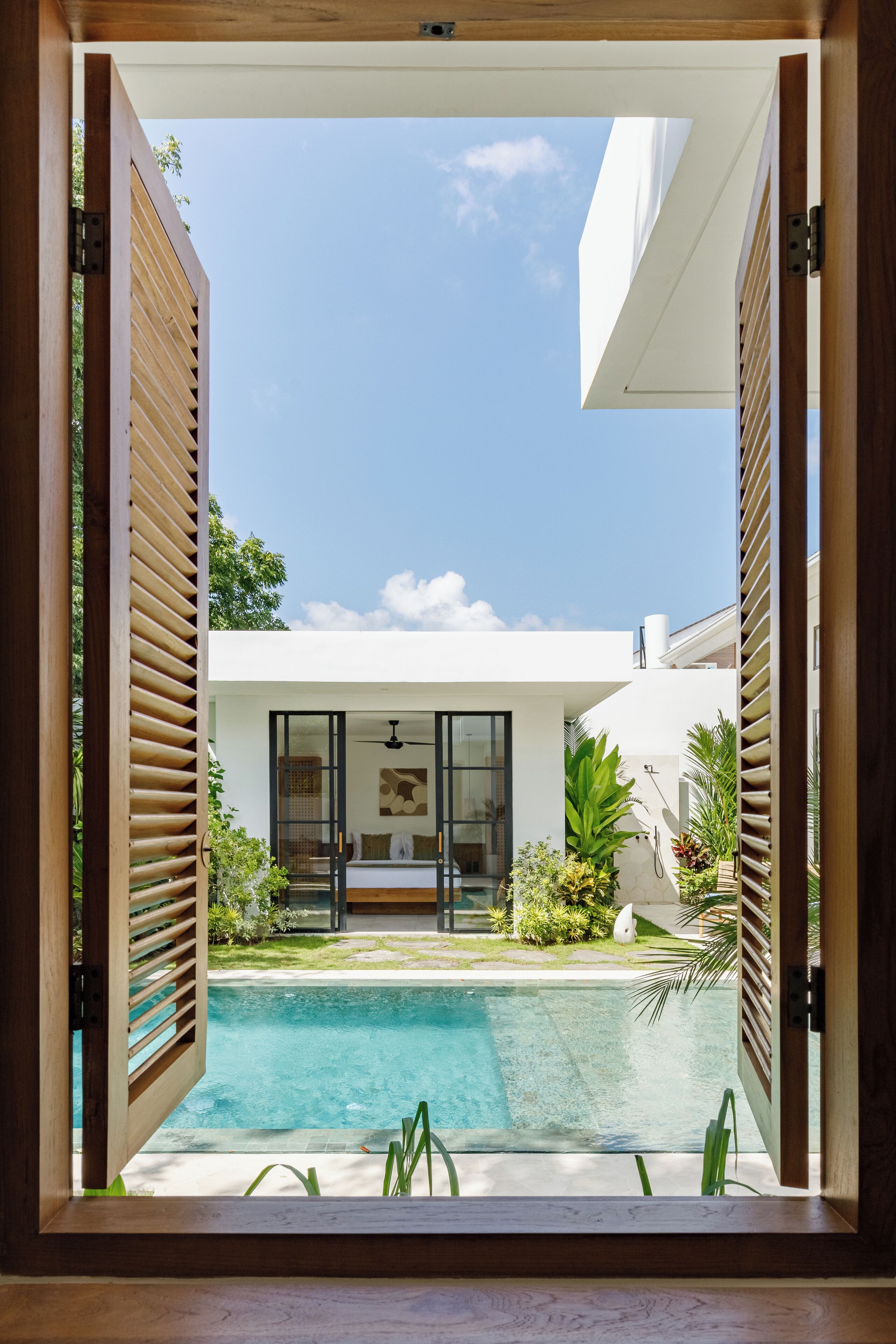 Una puerta de madera abierta que da a una casa moderna con piscina, patio y vista al cielo.