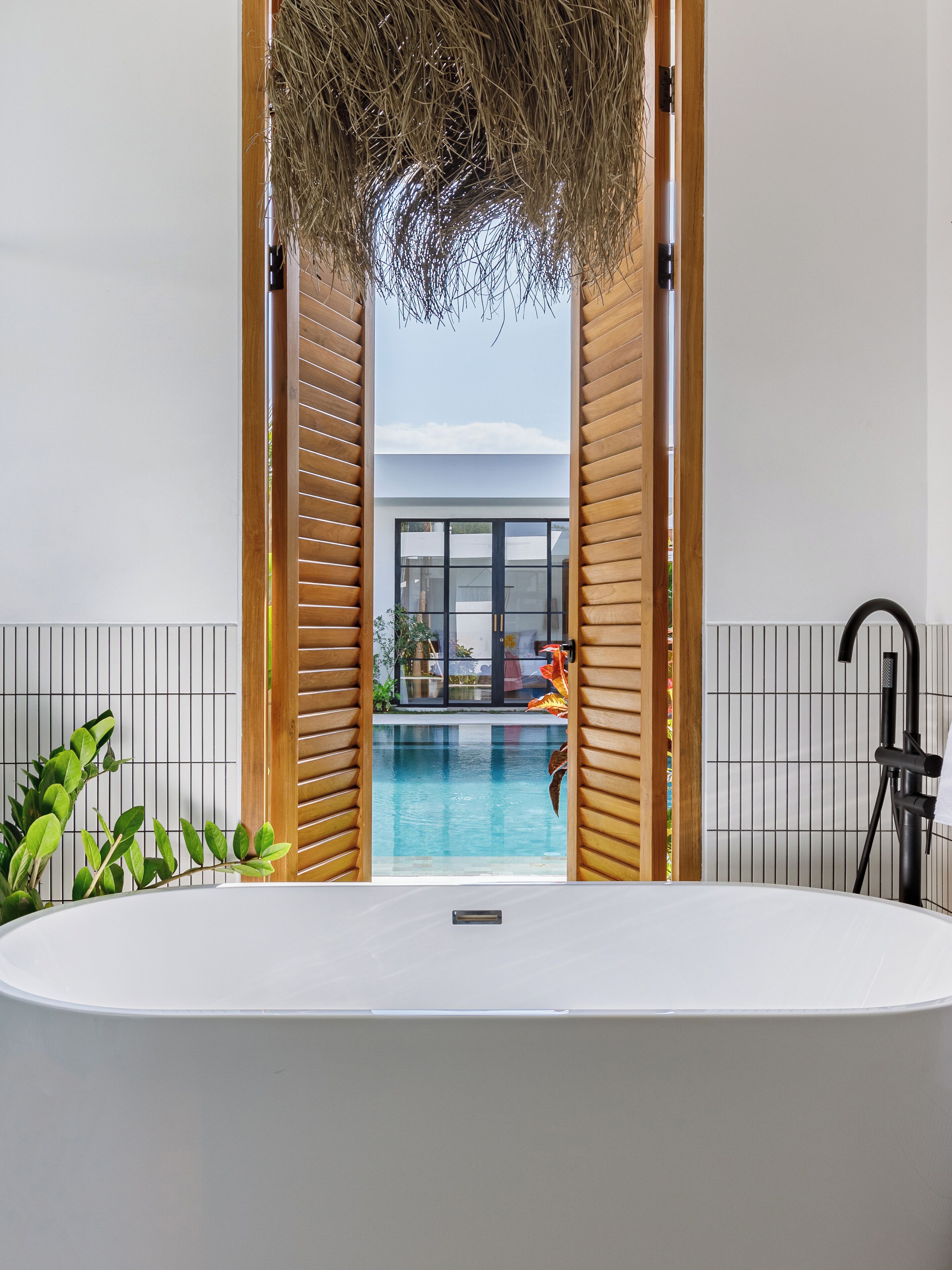 Un bagno moderno con una grande vasca, listelli in legno e vista su una piscina all'aperto.