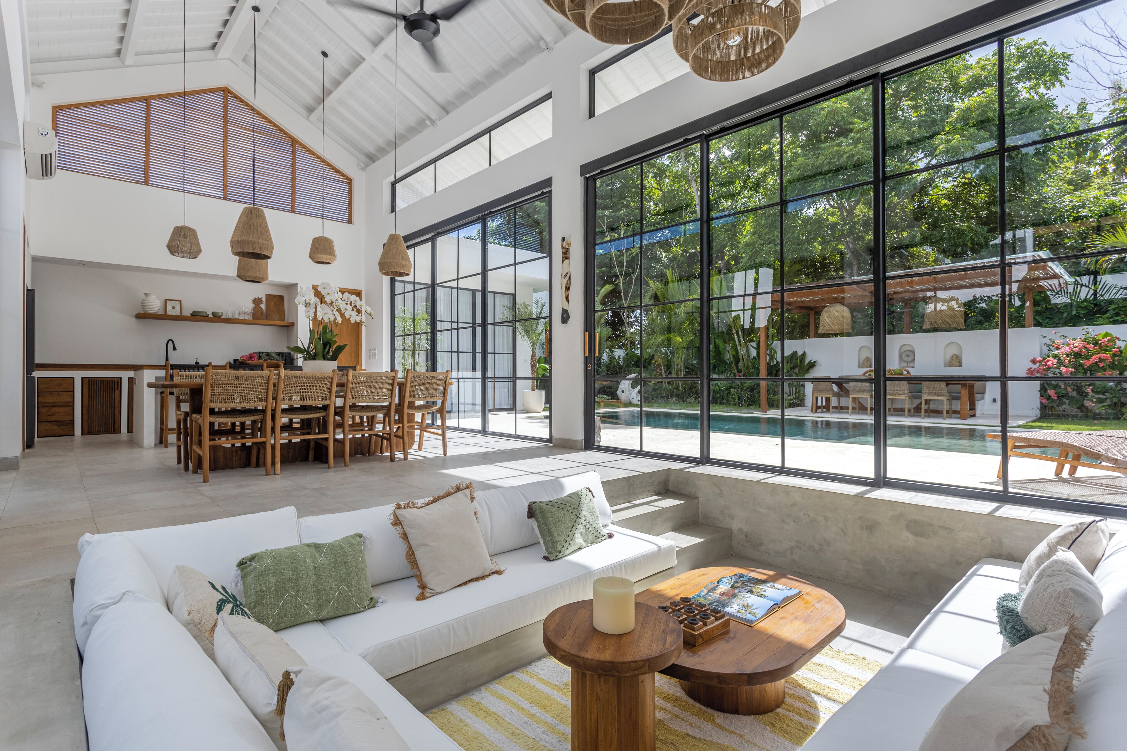 A spacious living area with a large sofa, a coffee table, and a dining area with wicker furniture.