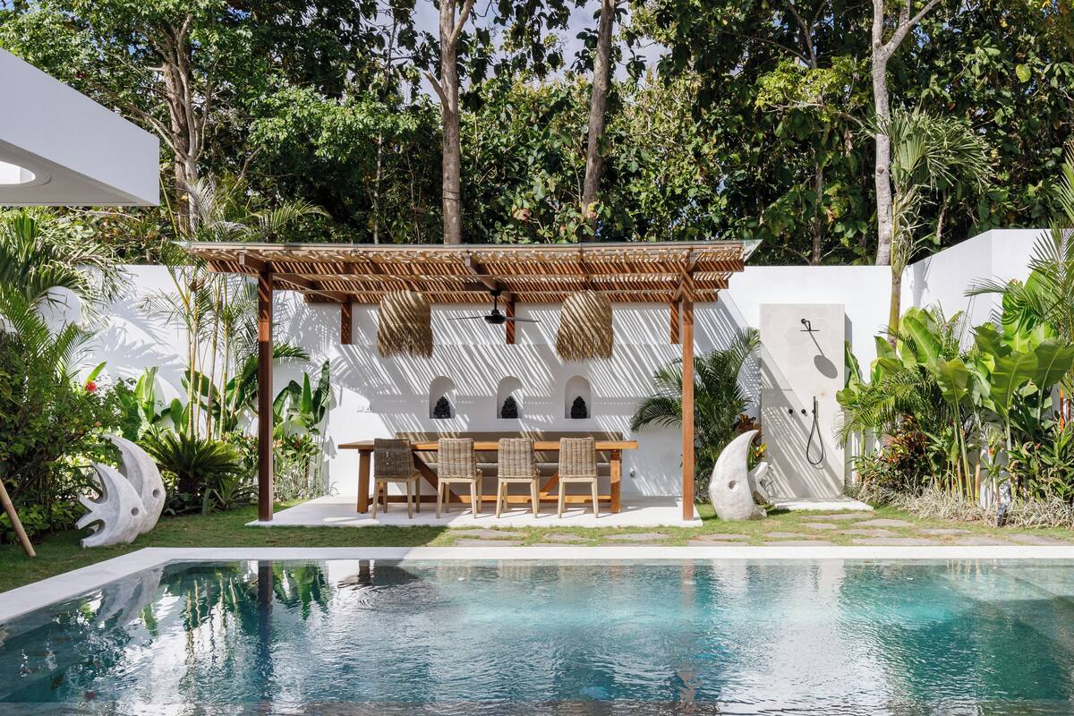 A poolside area with a pergola, seating, and a white wall with decorative elements.
