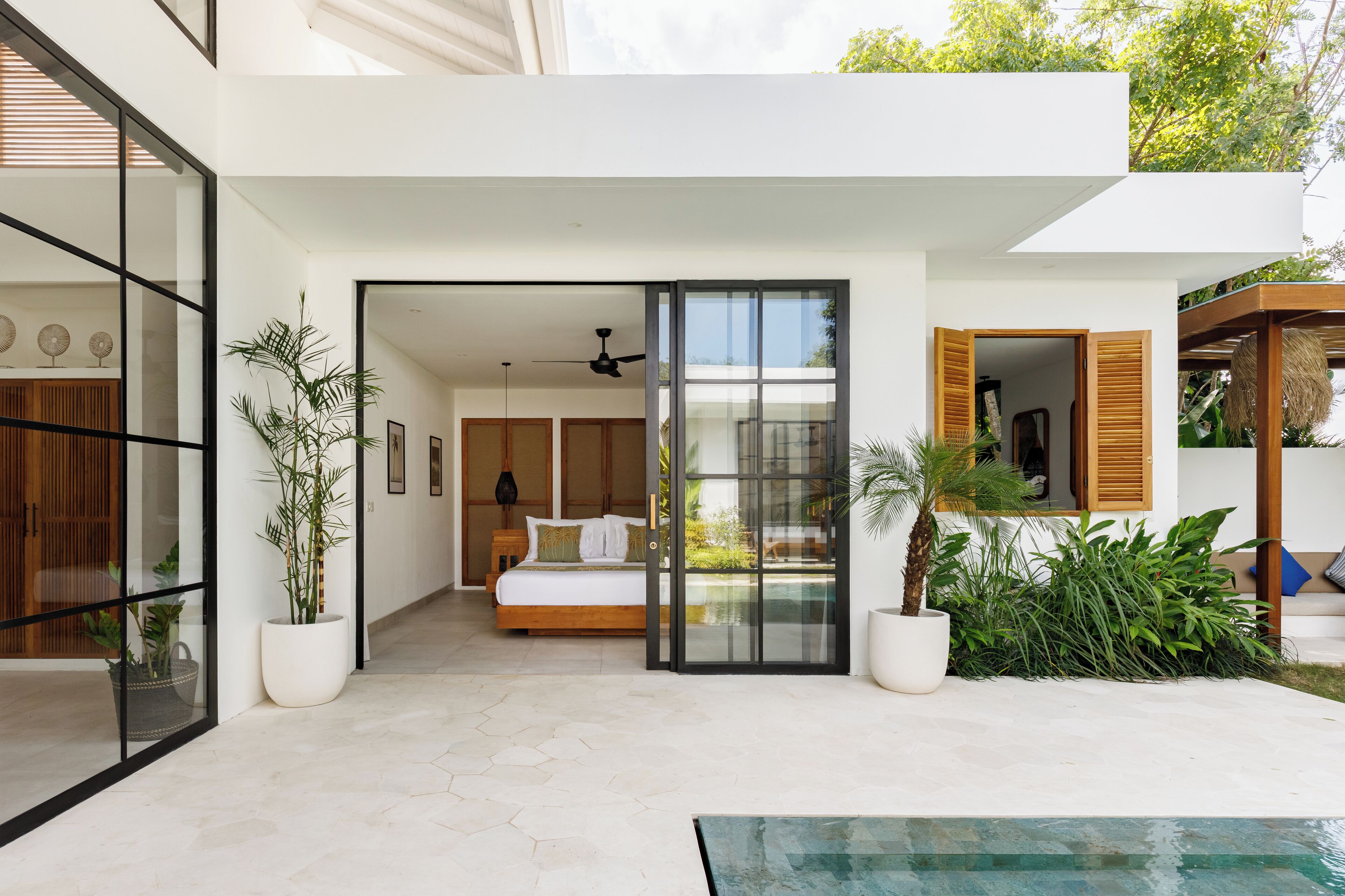 A modern, open-plan living area with a large bed, sliding glass doors leading to a bedroom, and a pool area.