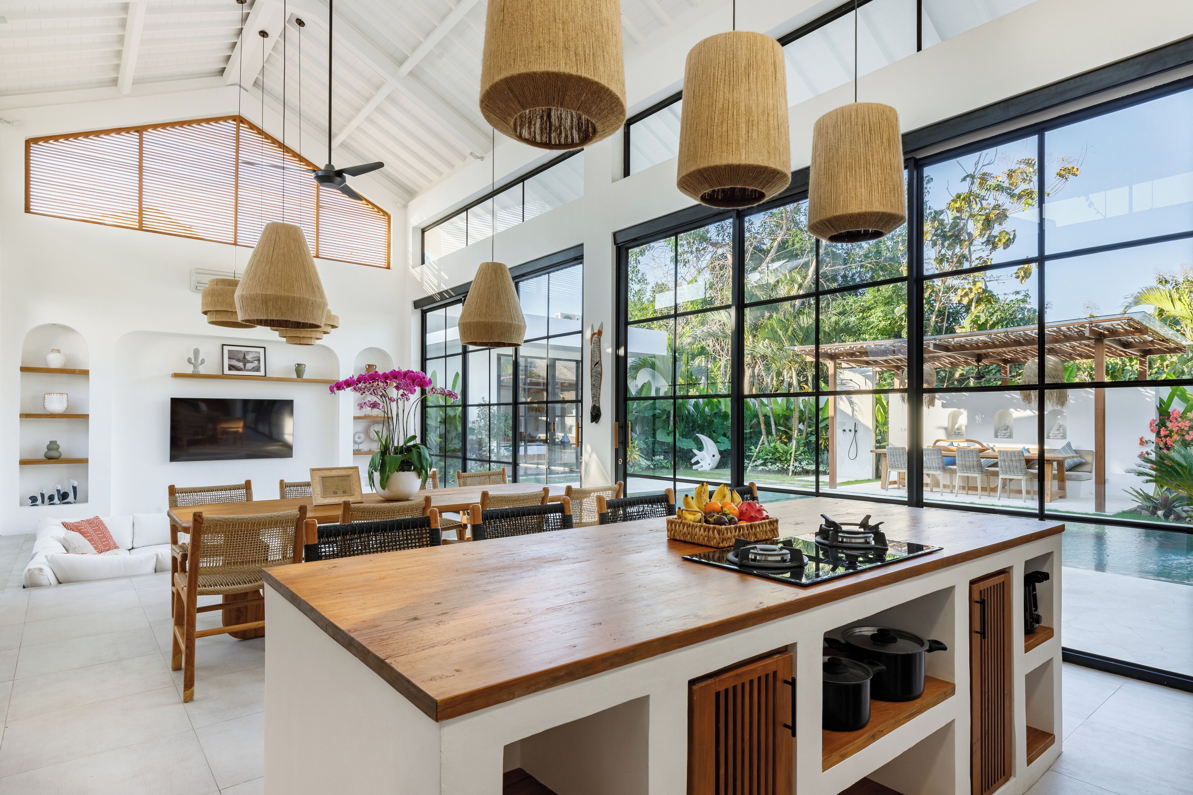 Une cuisine spacieuse avec un îlot central en bois, de grandes fenêtres et des lampes suspendues en osier.