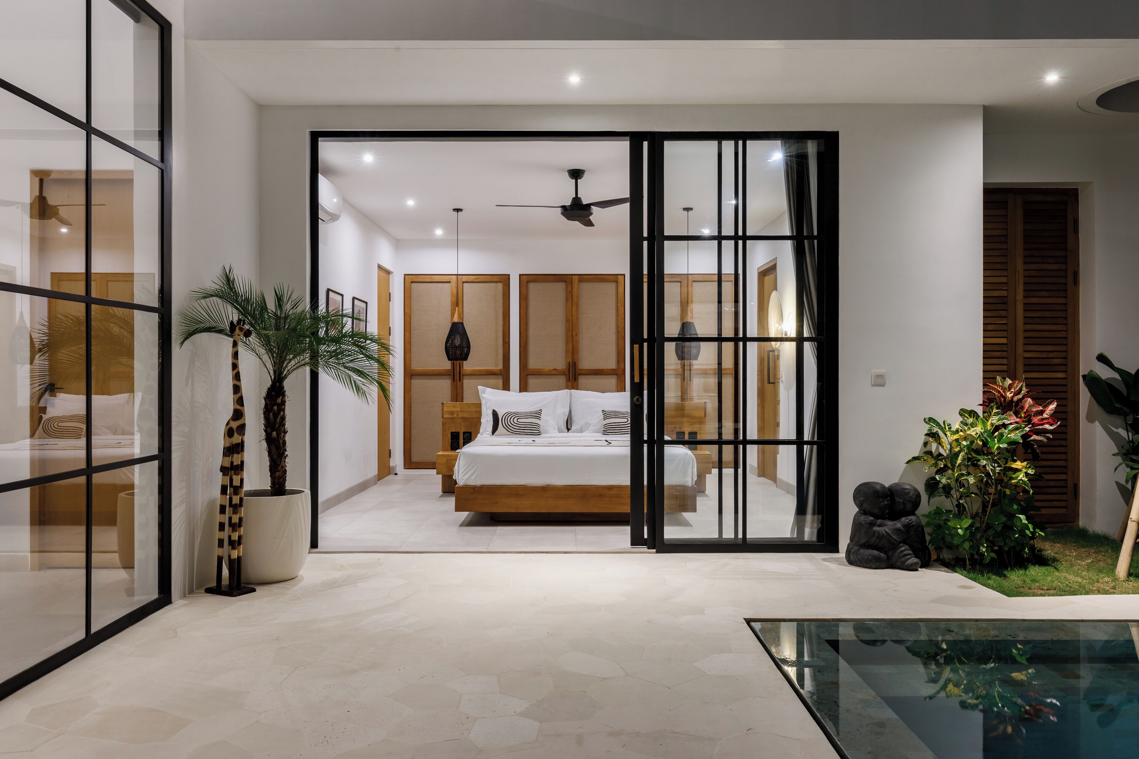 A modern bedroom with a large bed, a ceiling fan, and a glass door leading to a bathroom.