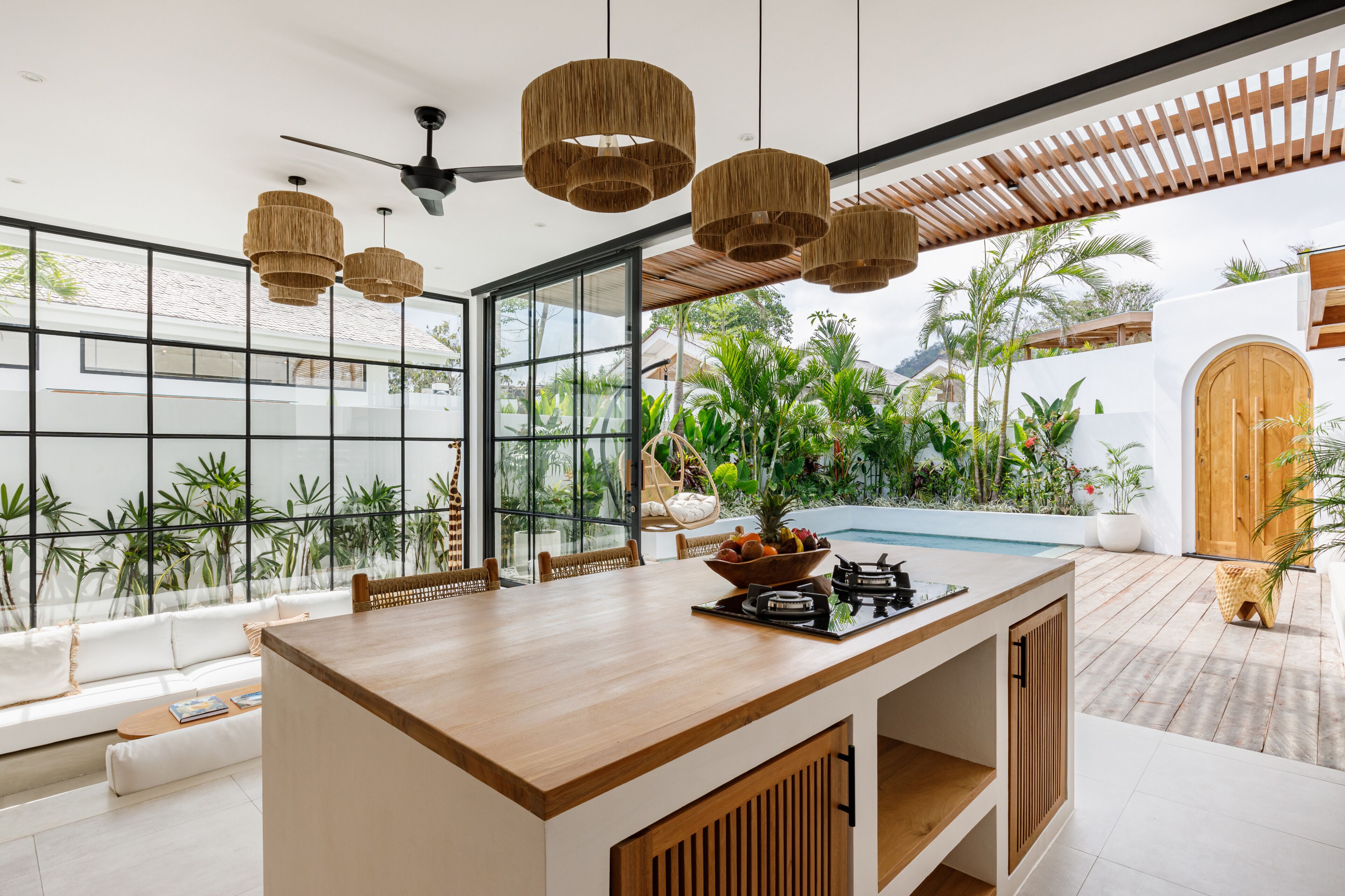 A modern kitchen with a wooden island, large windows, and a view of a pool and greenery.