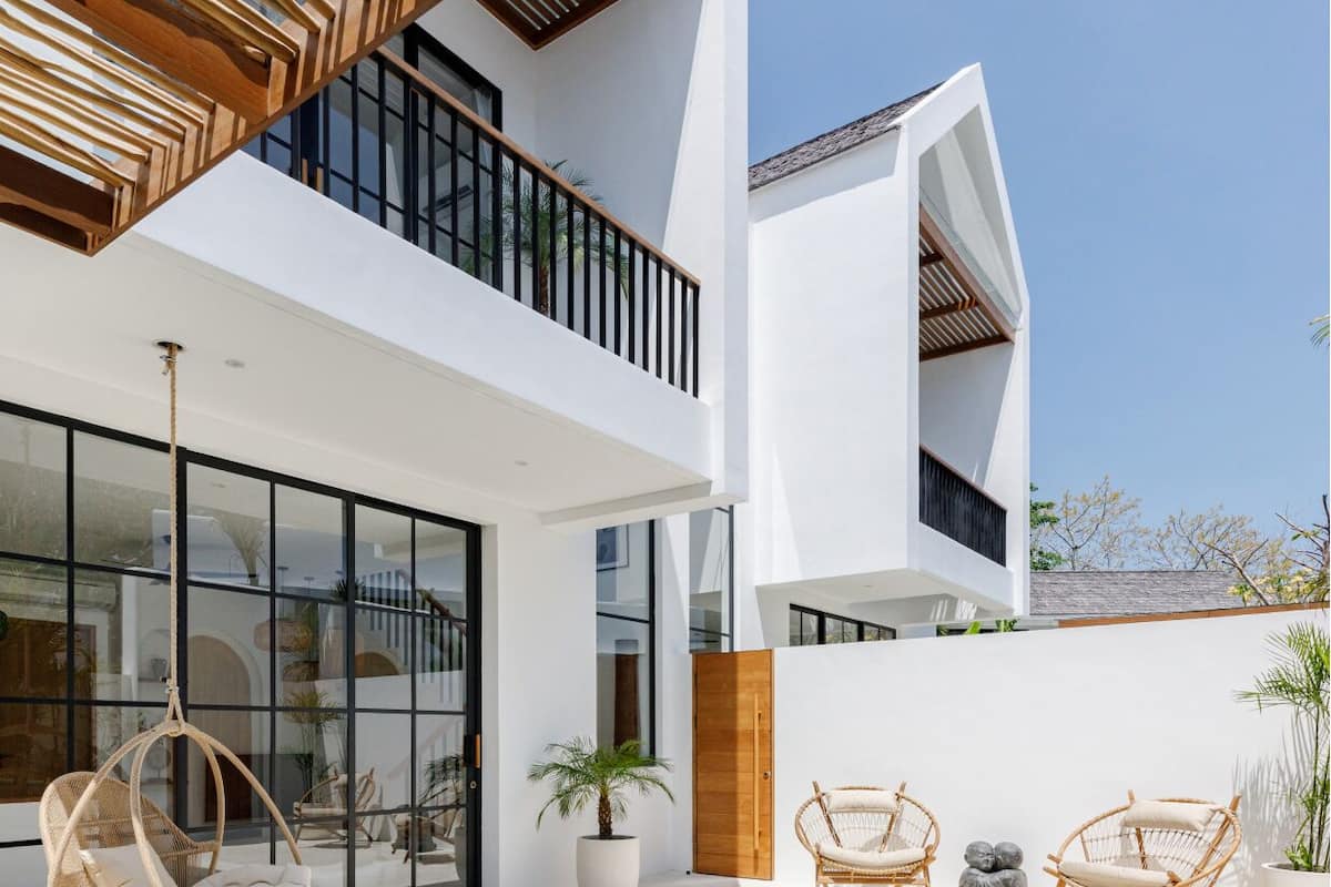A modern house with a swimming pool, wicker chairs, and a potted plant.