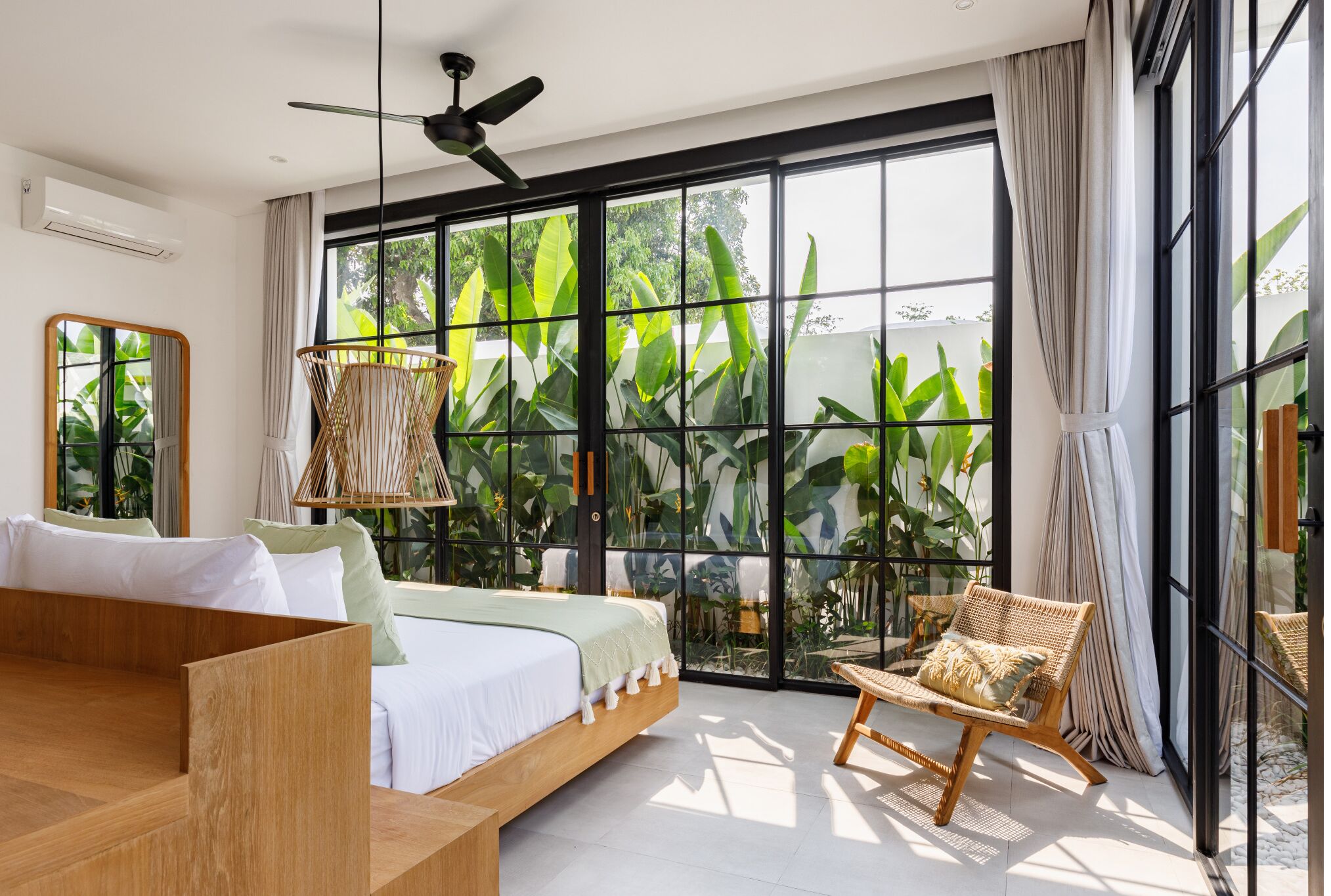 Ein modernes Schlafzimmer mit einem großen Fenster, einem Deckenventilator, einem Bett mit Holz Kopfteil und einem Korbstuhl.