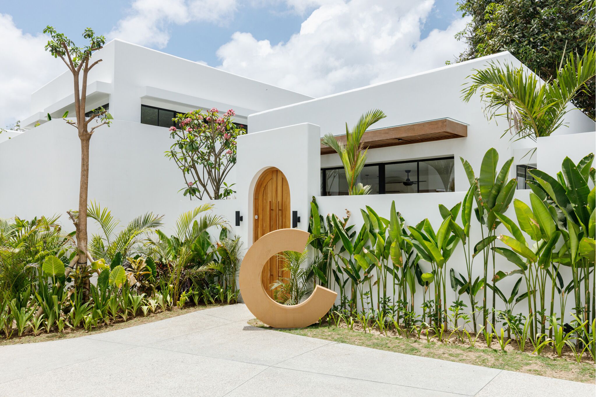 Un edificio moderno con una gran puerta de madera, rodeado de exuberante vegetación tropical.