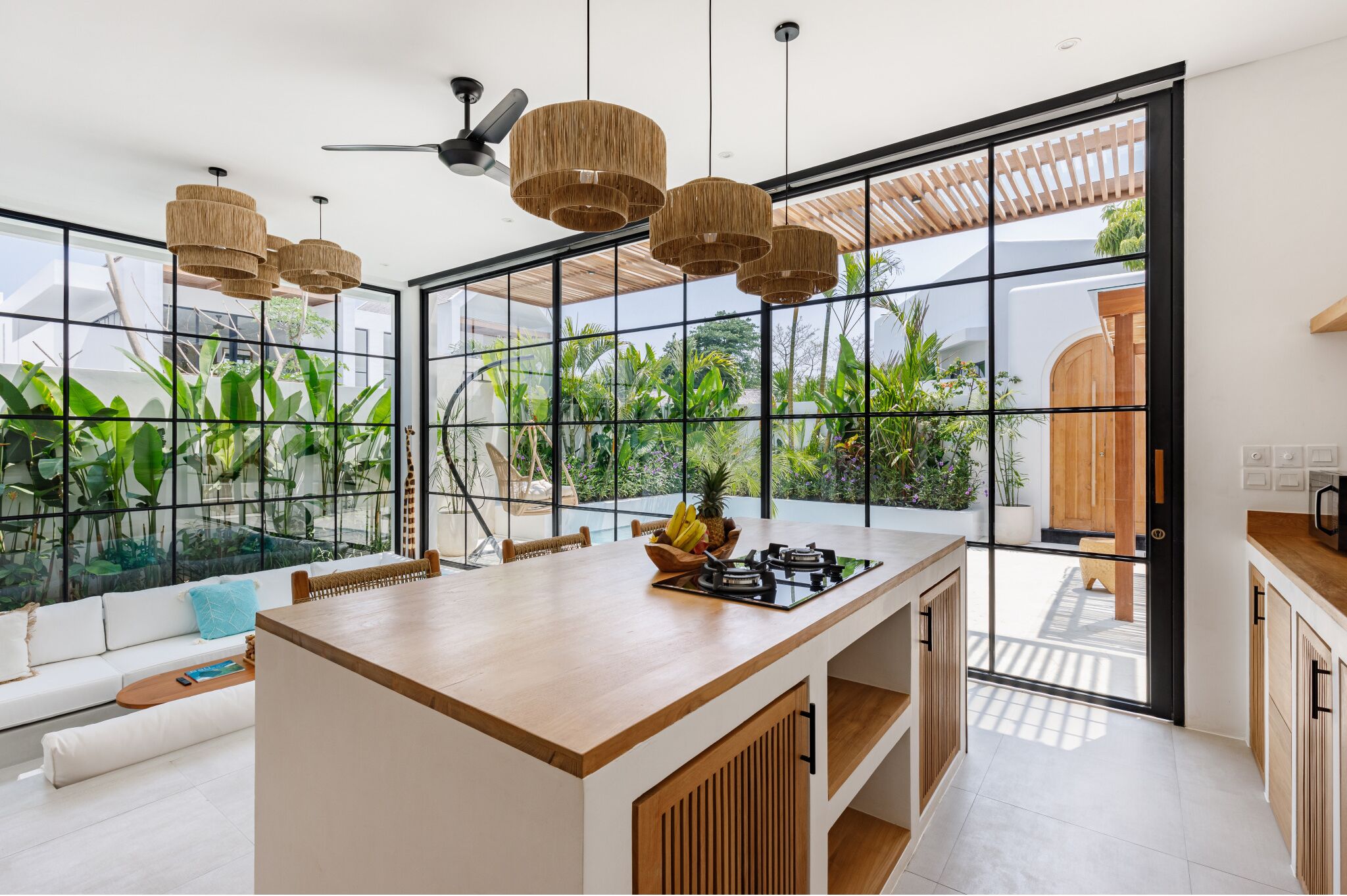 A modern kitchen with a central island, large windows, and a view of greenery outside.