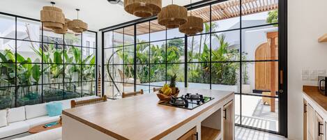 A modern kitchen with a central island, large windows, and a view of greenery outside.