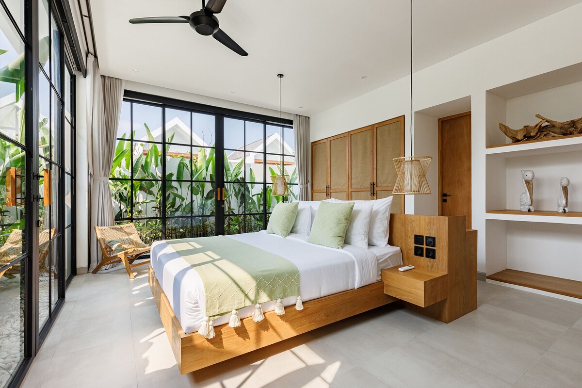 Un dormitorio moderno con una cama grande, cabecero de madera y vistas a zonas verdes.