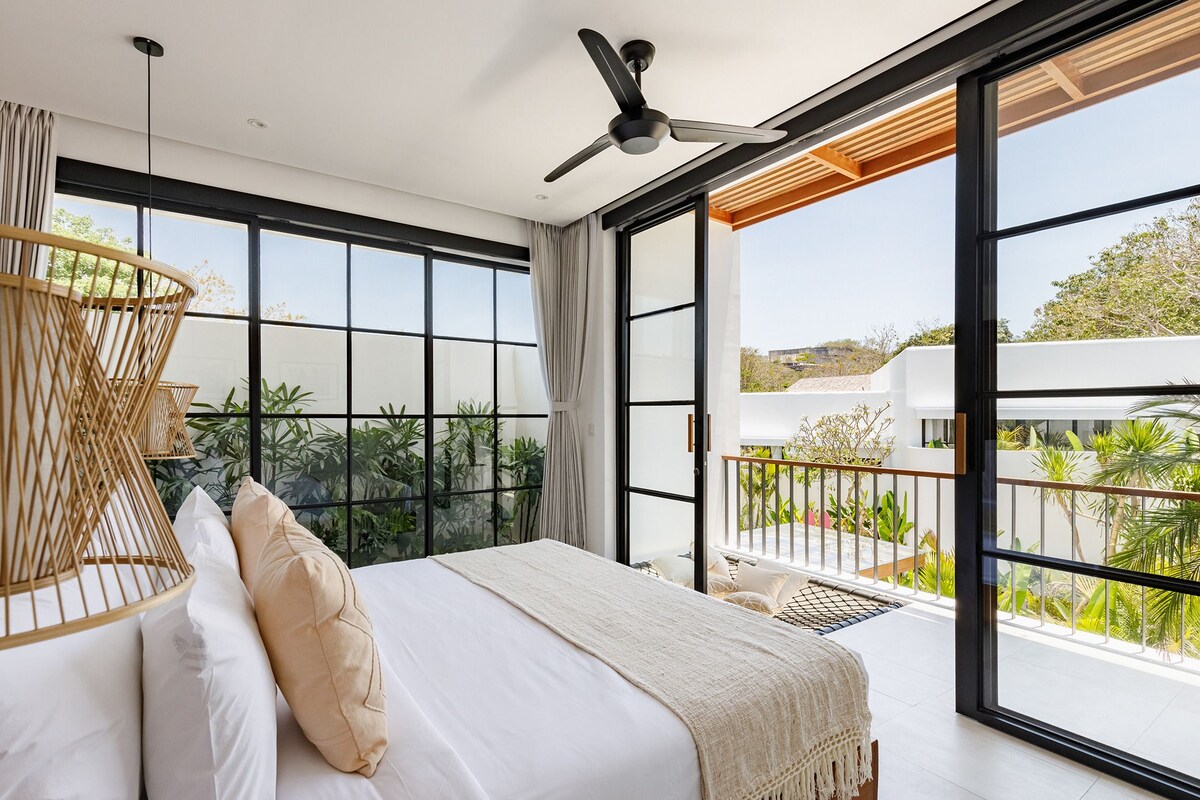 Un dormitorio con una cama grande, un ventilador de techo y un balcón con vista a zonas verdes.