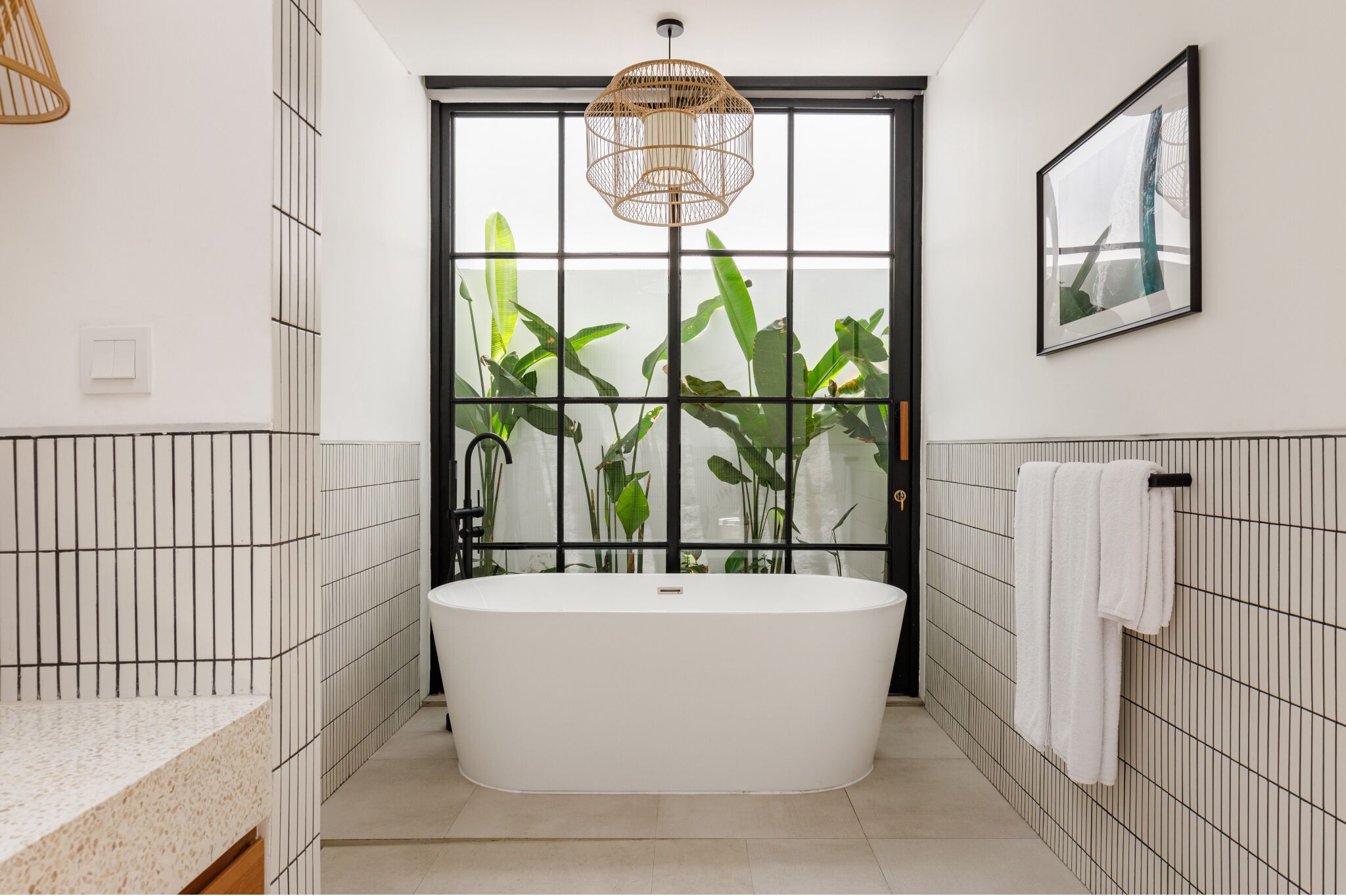 Une salle de bain moderne avec une baignoire sur pieds, une grande fenêtre agrémentée de plantes et un luminaire suspendu.