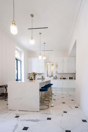 Un'ampia cucina con mobili bianchi, un'isola in marmo e sgabelli da bar blu.