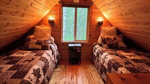 A cozy attic bedroom with two beds, a window, and a small table. - Rustic and cozy cabin with all new amenities near beautiful Hatcher’s Pass (Palmer)