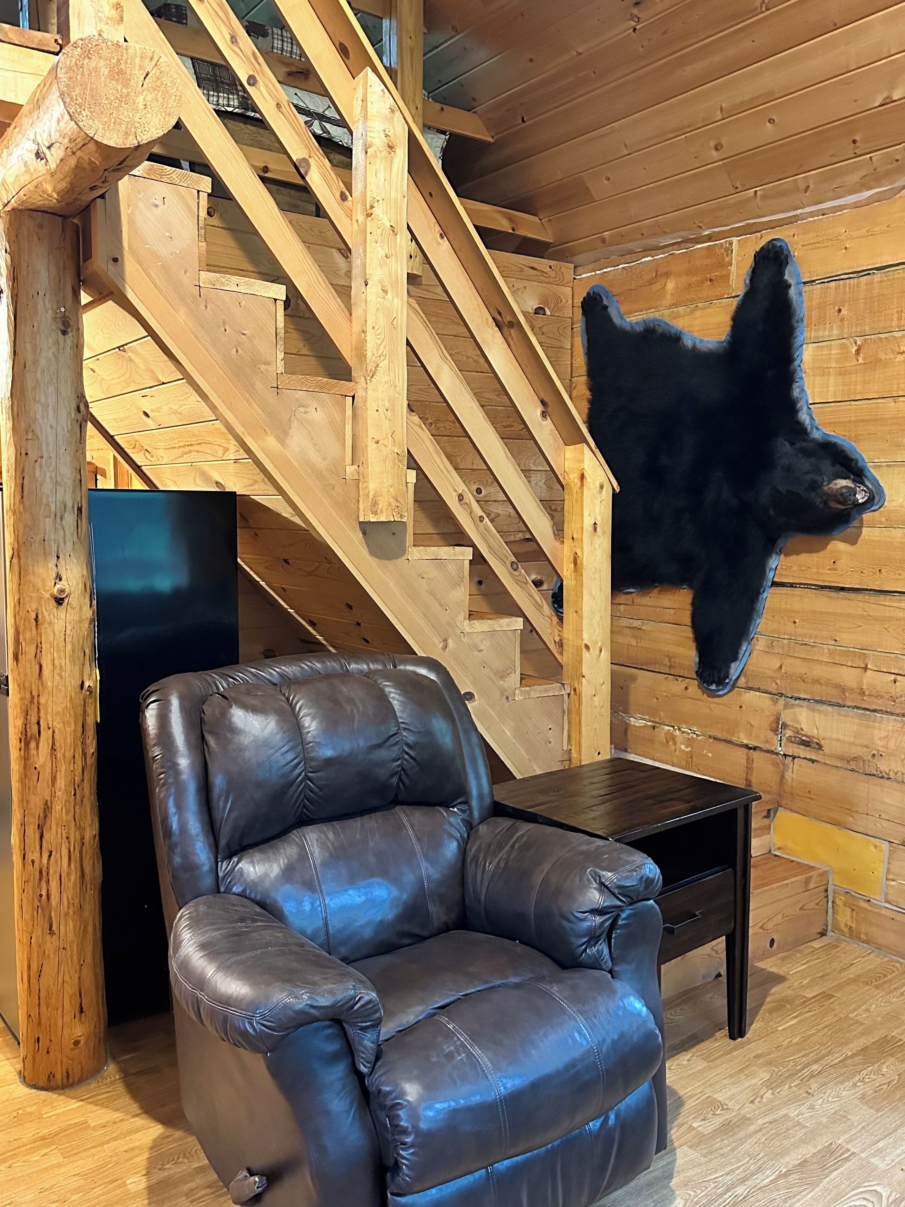 Een houten trap, een leren fauteuil en een zwarte bontjas aan de muur.
