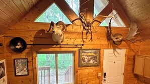A log cabin interior with a wooden ceiling, a black leather sofa, mounted animal heads, and a framed picture of Alaskan freshwater marshes. - Rustic and cozy cabin with all new amenities near beautiful Hatcher’s Pass (Palmer)