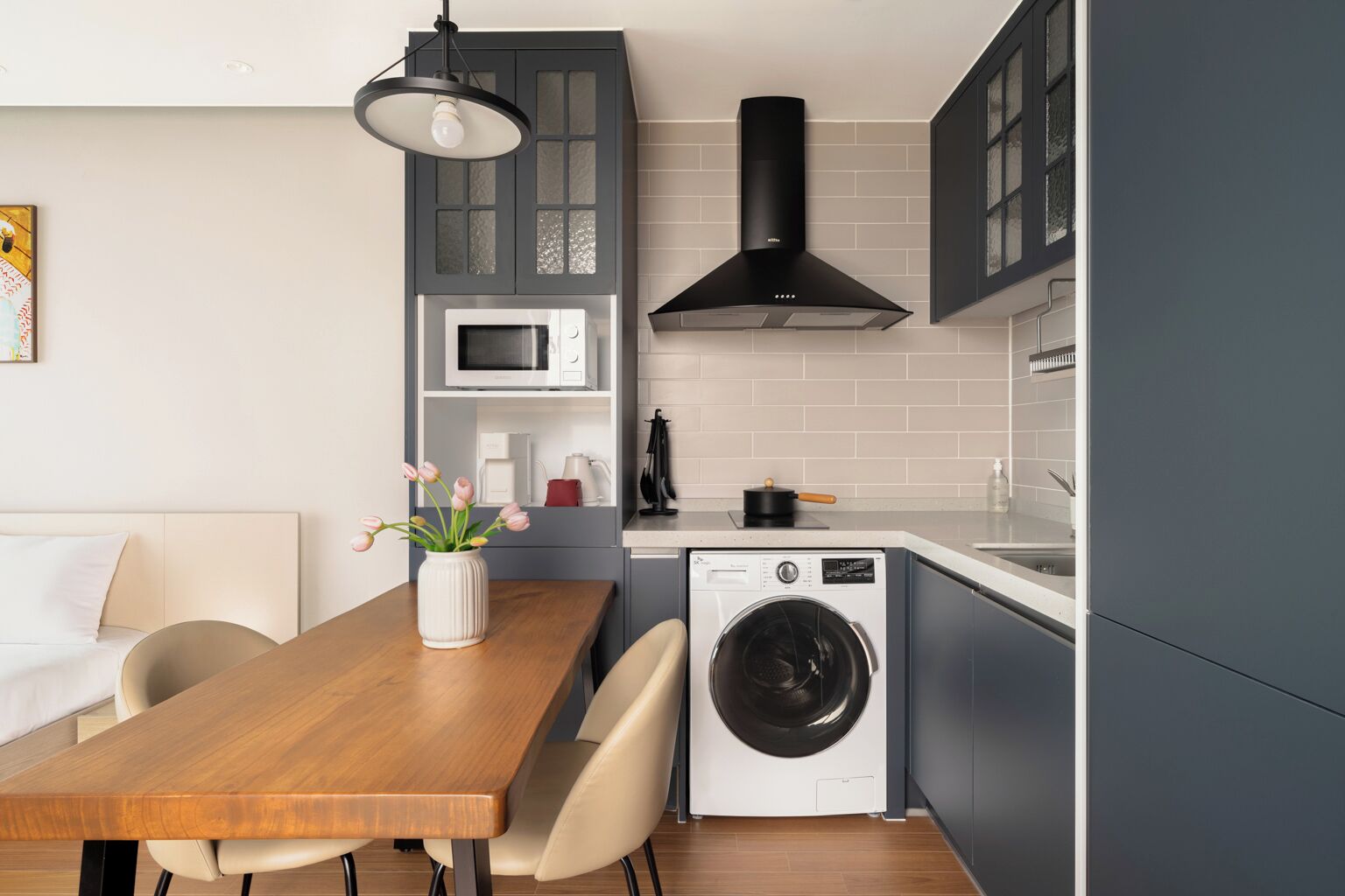 A modern kitchen with a built-in washing machine, grey cabinets, and a wooden dining table.