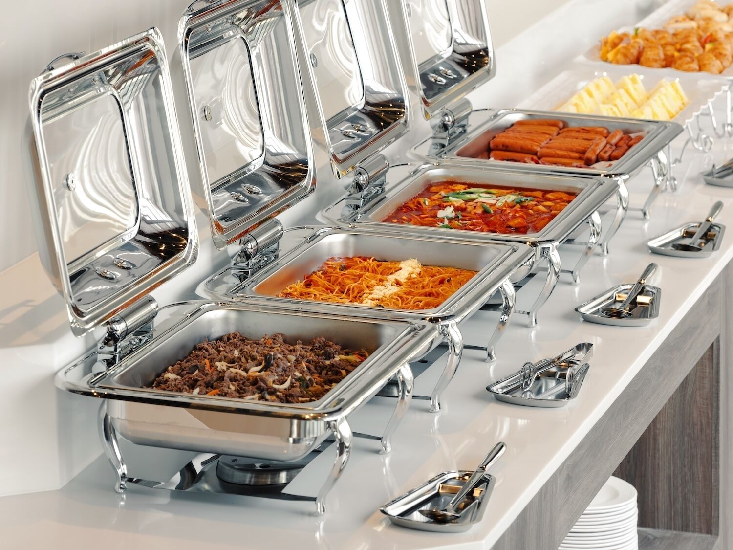 A buffet with various dishes in metal containers, including pasta, meat, and vegetables.