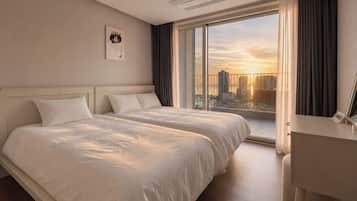 Habitación de hotel con dos camas, un ventanal amplio con vista a la ciudad, una mesita de noche y un cabecero.