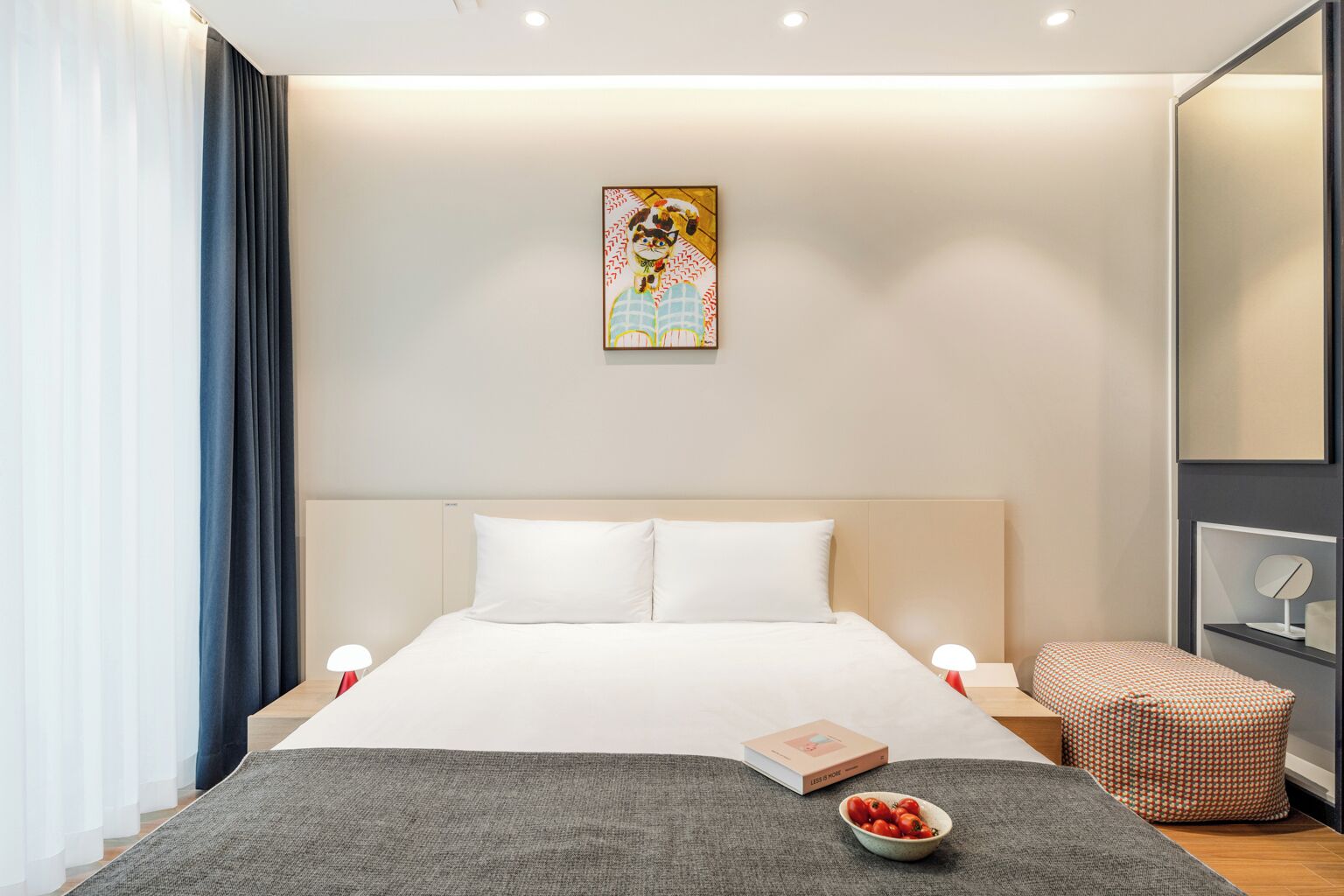 A modern hotel room with a large bed, bedside tables, a small seating area, and a painting on the wall.