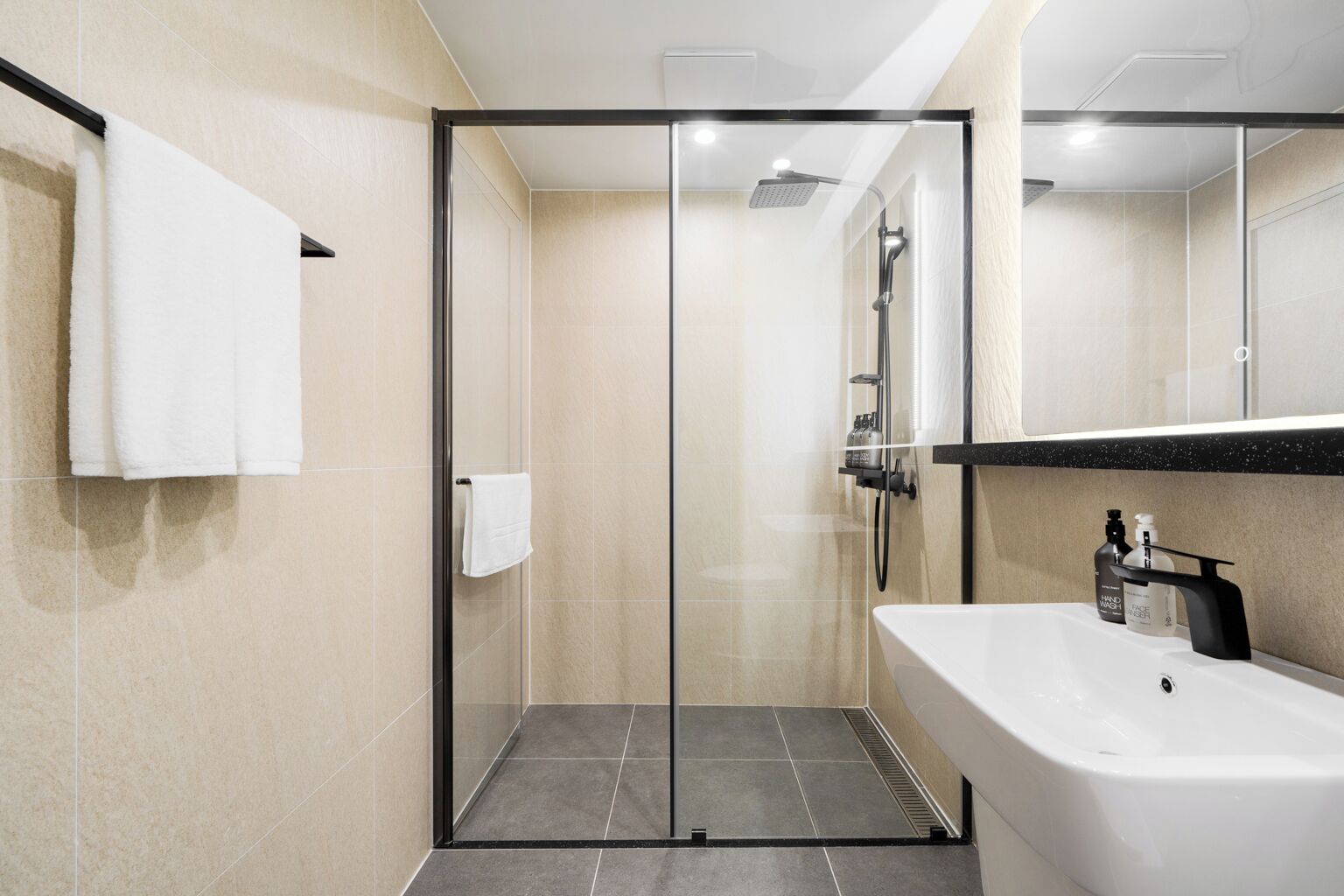 Un baño moderno con ducha de vidrio, un lavabo blanco y un espejo encima.