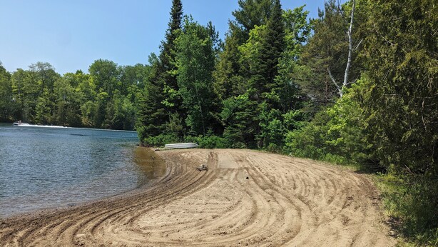 Une plage de sable avec un bateau sur l’eau, entourée d’une forêt dense.