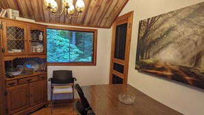 Un coin repas en bois, avec une table et des chaises, une fenêtre donnant sur une forêt et un buffet contenant de la vaisselle.