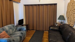 Un salon avec un plafond en bois, un téléviseur posé sur un meuble, un canapé, une table basse et un élément décoratif mural.