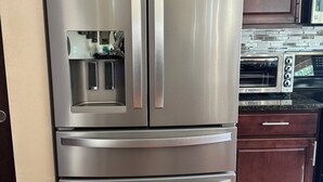 A stainless steel refrigerator with a water and ice dispenser, a microwave above it, and a toaster oven to the right.