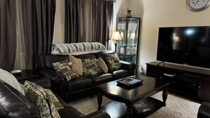 A living room with a black leather sofa, a coffee table, a flat-screen TV, and a glass cabinet with decorative items.