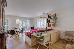 Een moderne, open woonruimte met een eethoek, een werkplek met bureau en planken, en een gezellig bedgedeelte.