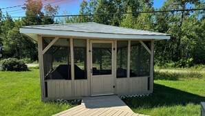 Un belvédère en bois doté d’une terrasse couverte, entouré de pelouse et d’arbres.