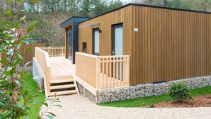 A modern wooden cabin with a wooden deck, a small staircase, and a stone wall foundation. - Modern Chalet With Dishwasher, in a Holiday Park, in a Natural Environment (Parc Hosingen)