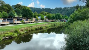 A lakeside accommodation area with modern cabins, a walking path, and a forested backdrop. - Modern Chalet With Dishwasher, in a Holiday Park, in a Natural Environment (Parc Hosingen)