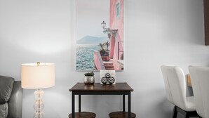 Ein Zimmer mit einem Tisch, zwei Stühlen, einer Lampe, einem gerahmten Bild und einem Blumentopf.