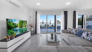 A modern living room with a flat-screen TV, a sofa, a coffee table, and a view of a pool and outdoor seating area. - Gorgeous home in Sevid (Sevid)