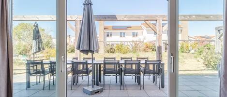 A room with a sliding glass door leading to an outdoor patio with a table and chairs, a covered umbrella, and a view of a residential area.