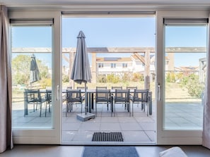 A room with a sliding glass door leading to an outdoor patio with a table and chairs, a covered umbrella, and a view of a residential area. - Villa Near Noordwijk Beach (Noordwijkerhout)
