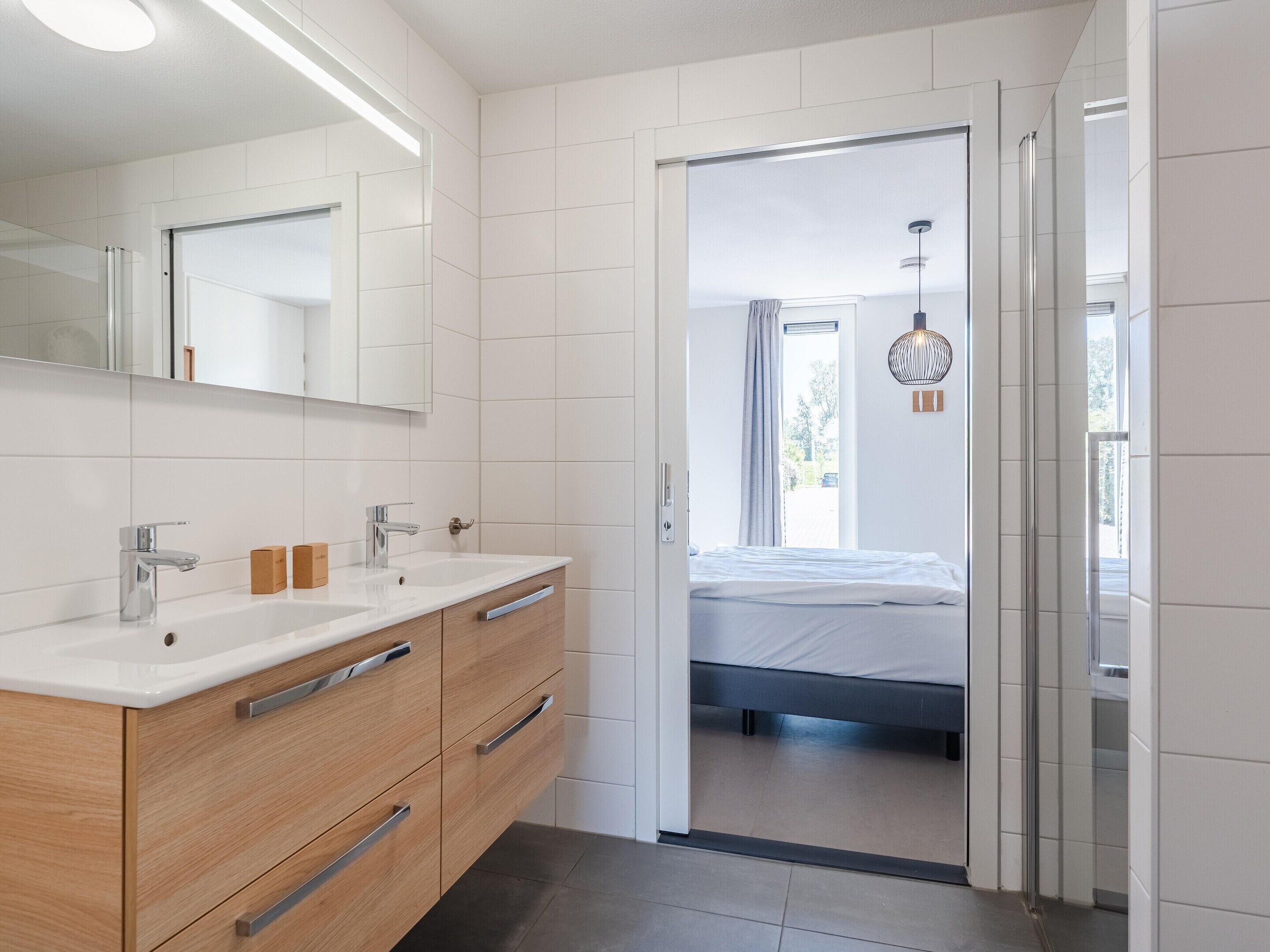 A modern bathroom with a double sink, wooden vanity, and a large mirror.