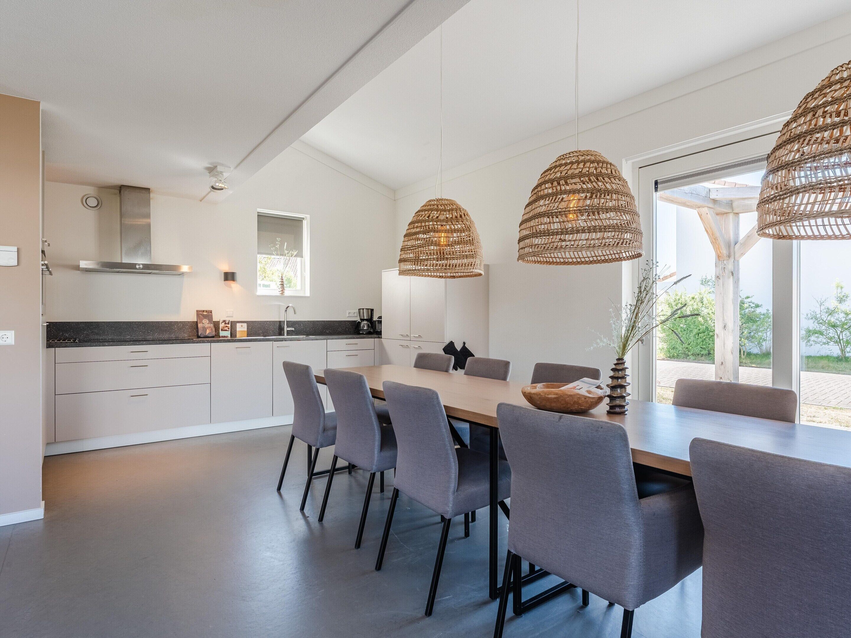 Una cucina moderna con mobili bianchi, un piano di lavoro nero e un'area pranzo con sedie grigie e un tavolo in legno.