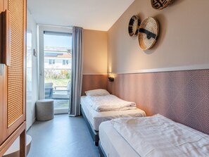 A hotel room with two beds, a window with curtains, a wall-mounted light, and a view of the outside.
