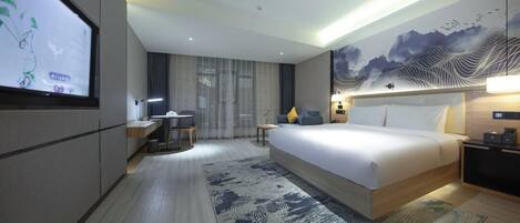 A modern hotel room with a large bed, a desk, a TV, and a wall with a mountain painting.