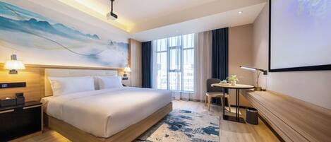 Una habitación de hotel moderna con una cama grande, un escritorio y un ventanal amplio.
