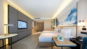 Une chambre d’hôtel moderne avec deux lits, un bureau, une télévision et un grand tableau au mur.